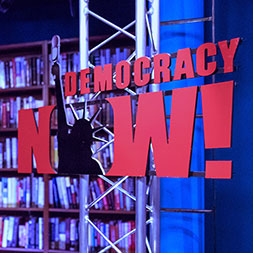 Democracy Now sign. Links to What to Give
